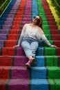 Young woman wearing casual clothes and sunglasses sits on rainbow painted stairs Royalty Free Stock Photo