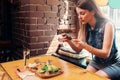 Young woman wearing casual clothes taking picture of her healthy lunch sitting on windowsill in trendy cafe Royalty Free Stock Photo