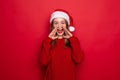 Young woman wearing christmas hat smiling happy scream isolated on red background