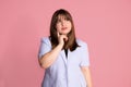 Young woman wearing classic business clothes on pink background put her hand to face, looks up, thoughtful portrait in studio on