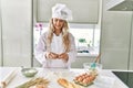 Young woman wearing cook uniform cracking egg on flour at kitchen