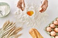 Young woman wearing cook uniform cracking egg on flour at kitchen