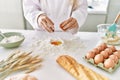 Young woman wearing cook uniform cracking egg on flour at kitchen