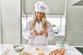 Young woman wearing cook uniform cracking egg on flour at kitchen