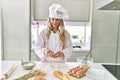 Young woman wearing cook uniform cracking egg on flour at kitchen