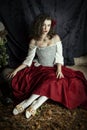 A young woman wearing a corset and red skirt and sitting in an opulent, vintage setting