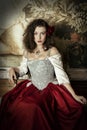 A young woman wearing a corset and red skirt and sitting in an opulent, vintage setting Royalty Free Stock Photo