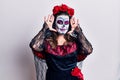 Young woman wearing day of the dead costume over white smiling cheerful playing peek a boo with hands showing face