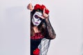 Young woman wearing day of the dead custome holding blank empty banner making fun of people with fingers on forehead doing loser