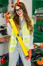 Young woman wearing denim jumpsuit and glasses with long hair holding in hands spirit level and smiling. Royalty Free Stock Photo