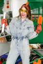 Young woman wearing denim jumpsuit and glasses with long hair holding in hands wrench and brush and smiling