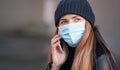 Young woman wearing disposable blue face mouth nose mask talking on mobile phone. Closeup detail, can be used during Royalty Free Stock Photo