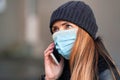 Young woman wearing disposable blue virus face mouth nose mask talking on mobile phone. Closeup detail, can be used during Royalty Free Stock Photo