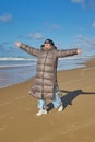 A young woman wearing a down jacket enjoys the warmth of the sun while walking along the sandy ocean beach Royalty Free Stock Photo