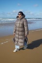 A young woman wearing a down jacket enjoys the warmth of the sun while walking along the sandy ocean beach Royalty Free Stock Photo