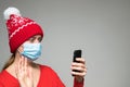 Young woman wearing face mask and Christmas red hat making video call by smart phone Royalty Free Stock Photo