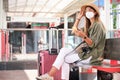 Young woman wearing face mask and a hat, using her smartphone while is waiting for the train at a train station Royalty Free Stock Photo