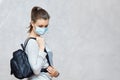 Young woman wearing flu mask and casual clothes stands with black leather backpack, going to walk outside, looking down with sad e Royalty Free Stock Photo