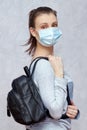 Young woman wearing flu mask and casual clothes stands with black leather backpack, going to walk outside. Royalty Free Stock Photo