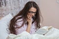 Young woman wearing glasses while reading book in bed. Relaxed woman lying in bed in sleepwear reading a book. Royalty Free Stock Photo