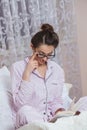 Young woman wearing glasses while reading book in bed. Relaxed woman lying in bed in sleepwear reading a book. Royalty Free Stock Photo