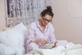 Young woman wearing glasses while reading book in bed. Relaxed woman lying in bed in sleepwear reading a book. Royalty Free Stock Photo