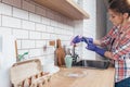 Young woman wearing glove cleaning sink, wiping faucet in kitchen Royalty Free Stock Photo