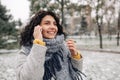 Young woman wearing grey coat and blue scarf talking on the mobile phone at a snowy winter park. Female stands with her smartphone Royalty Free Stock Photo