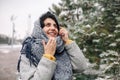 Young woman wearing grey coat and blue scarf talking on the mobile phone at a snowy winter park. Female stands with her smartphone Royalty Free Stock Photo