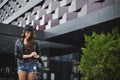 Young woman wearing a hat, leather jacket and denim shorts smiling in urban background. Model girl in casual clothes Royalty Free Stock Photo