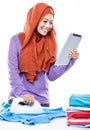 Young woman wearing hijab reading article on tablet while ironin Royalty Free Stock Photo