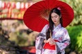 A young woman wearing a Japanese traditional kimono or yukata holding an umbrella is happy and cheerful in the park