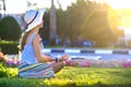 Young woman wearing light blue summer dress and yellow straw hat relaxing on green grass lawn in summer park. Girl in casual Royalty Free Stock Photo