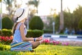 Young woman wearing light blue summer dress and yellow straw hat relaxing on green grass lawn in summer park. Girl in casual Royalty Free Stock Photo