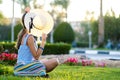 Young woman wearing light blue summer dress and yellow straw hat relaxing on green grass lawn in summer park. Girl in casual Royalty Free Stock Photo