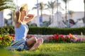 Young woman wearing light blue summer dress and yellow straw hat relaxing on green grass lawn in summer park. Girl in casual Royalty Free Stock Photo