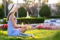 Young woman wearing light blue summer dress and yellow straw hat relaxing on green grass lawn in summer park. Girl in casual Royalty Free Stock Photo