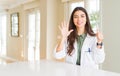 Young woman wearing medical coat at the clinic as therapist or doctor showing and pointing up with fingers number six while Royalty Free Stock Photo