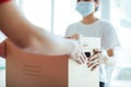 Young woman wearing medical mask receiving box from delivery man indoors.Prevention of virus spread