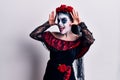 Young woman wearing mexican day of the dead makeup smiling cheerful playing peek a boo with hands showing face