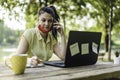 Young woman wearing open protective face mask using laptop outdoors - Female entrepreneur taking notes while calling with cell