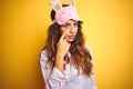 Young woman wearing pajama and sleep mask standing over yellow isolated background Pointing to the eye watching you gesture, Royalty Free Stock Photo