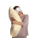 Young woman wearing pajamas and mask with pillow in sleepwalking state on white background