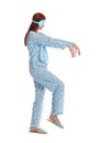 Young woman wearing pajamas, mask and slippers in sleepwalking state on white background