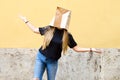 Young woman wearing a paper bag over her head in front of yellow Royalty Free Stock Photo