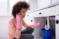 Woman Calling Plumber In Front Of Leaking From Sink Pipe