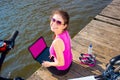 Young woman wearing in pink shirt sitting on the lake bridge using laptop computer