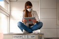 Young woman wearing a protective mask sitting on a big washing machine and using a tablet Royalty Free Stock Photo