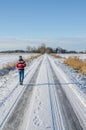 Young woman wearing red Norwegian jumper going for a winter walk with dog on snow covered road on a beautiful sunny day Royalty Free Stock Photo