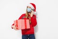 Young woman, wearing a red Santa Claus hat and a medical protective mask on her face, talking on a cell phone and holding a gift Royalty Free Stock Photo